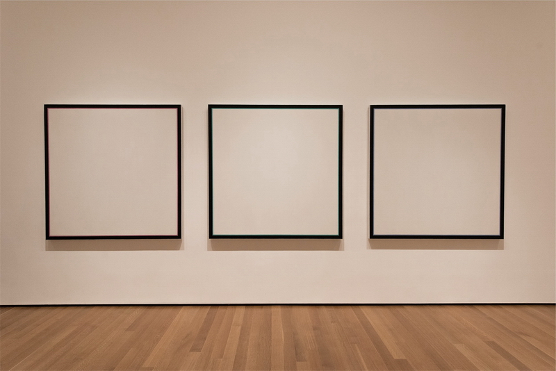 Leerer Kunstgalerie-Raum mit schwarzen, leeren Bilderrahmen an der off-tone-roséfarbenen Wand und mit Holzboden